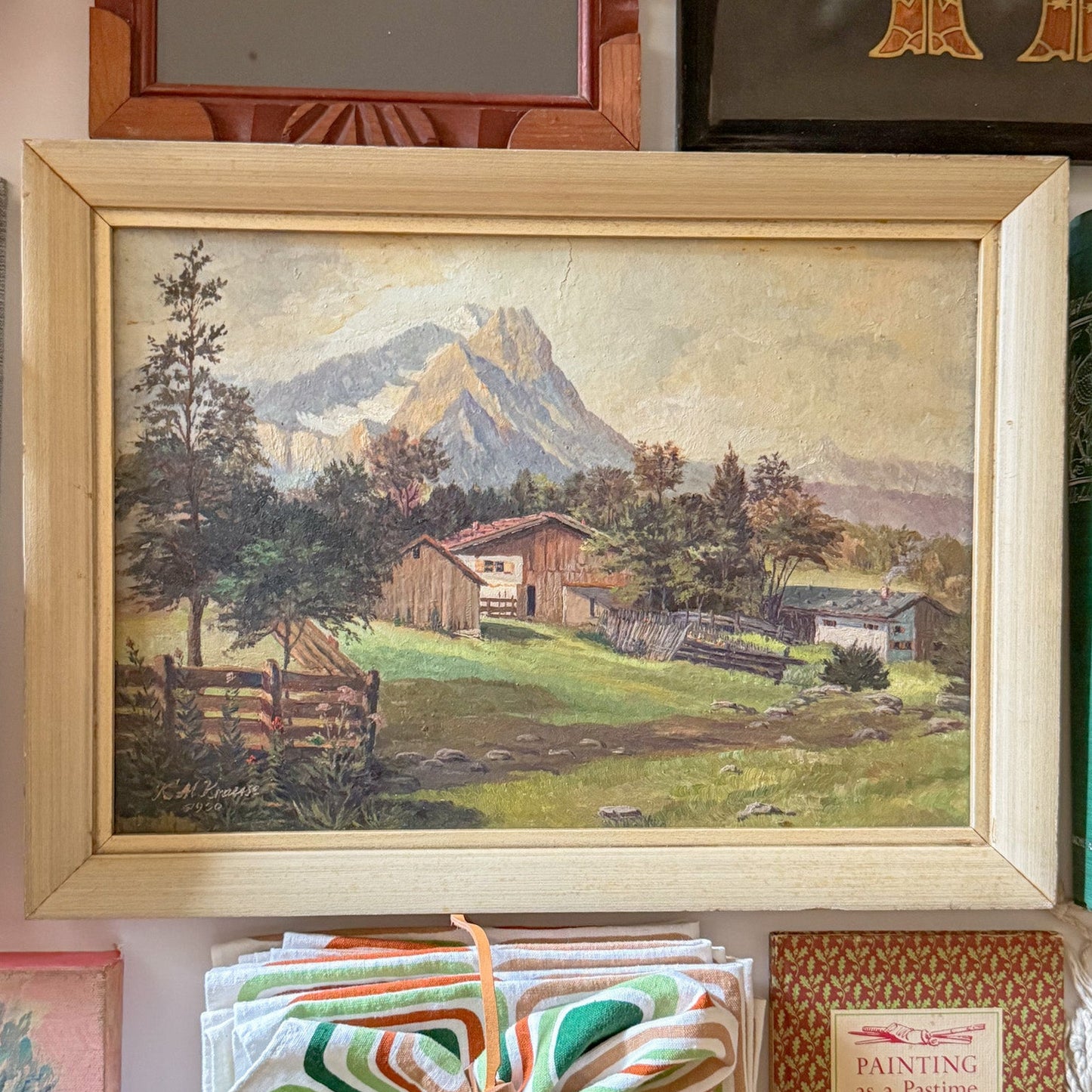 Framed landscape painting of a mountainous scene with a cabin, surrounded by other decorative items.